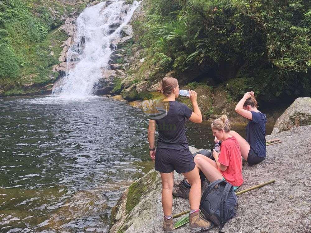 Hikers taking a rest by a majestic waterfall on a 2-day Tay Con Linh trekking tour