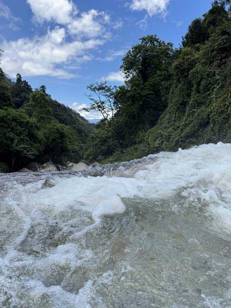 Fast clear water running over rock at Lung Vai Waterfall, forested valley beyond
