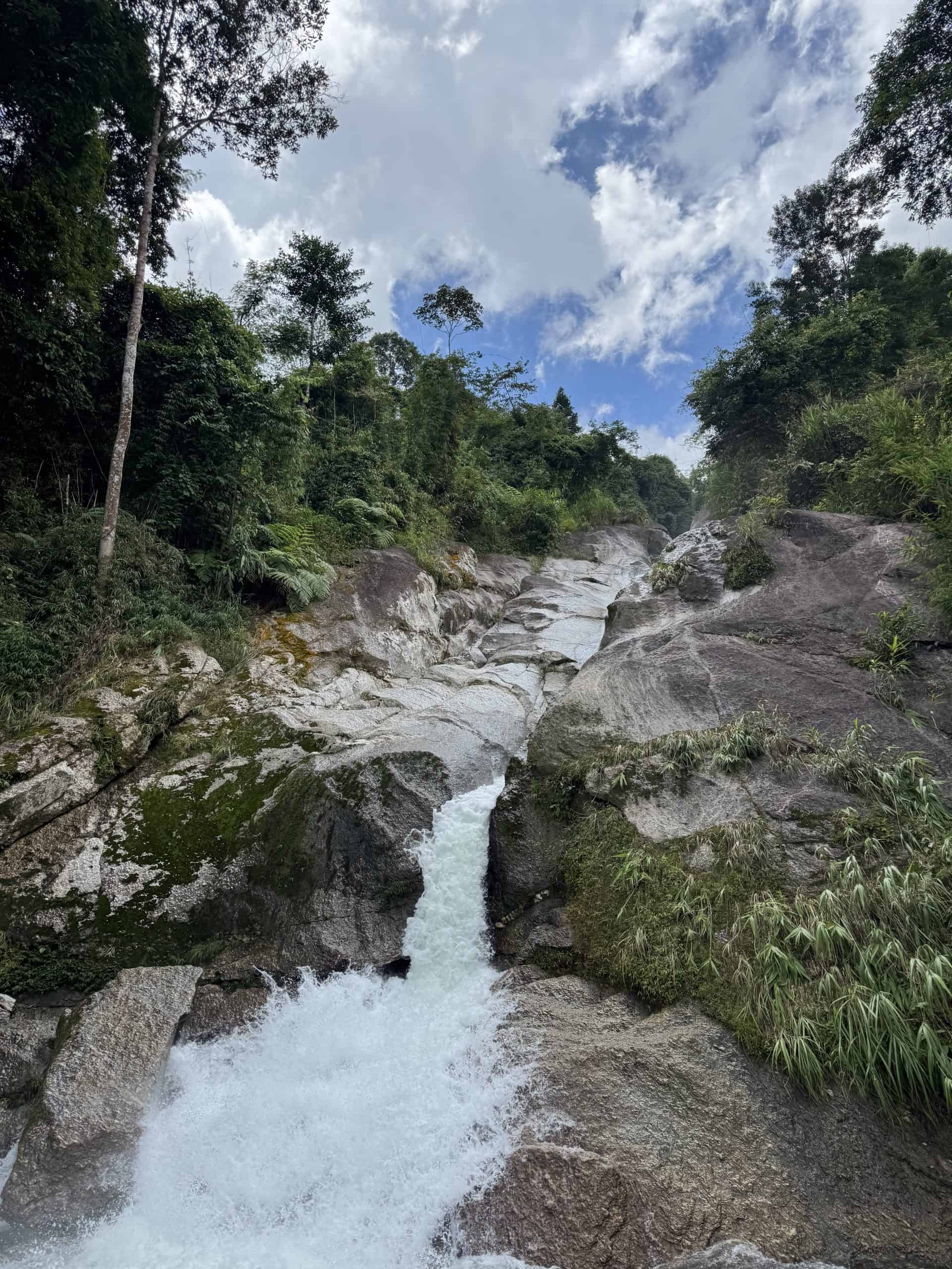 Lung Vai Waterfall falling over pale granite slabs under a blue sky, Tay Con Linh, Ha Giang