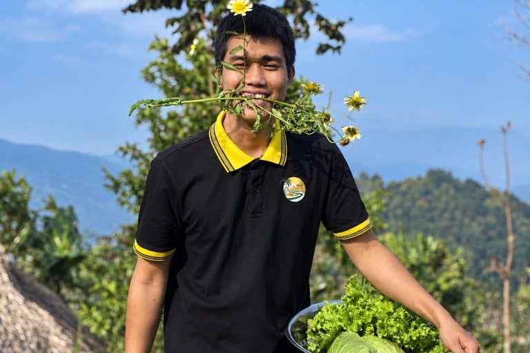 TVPalm team member smiling with a wild flower and a bowl of fresh greens from the Eco Garden