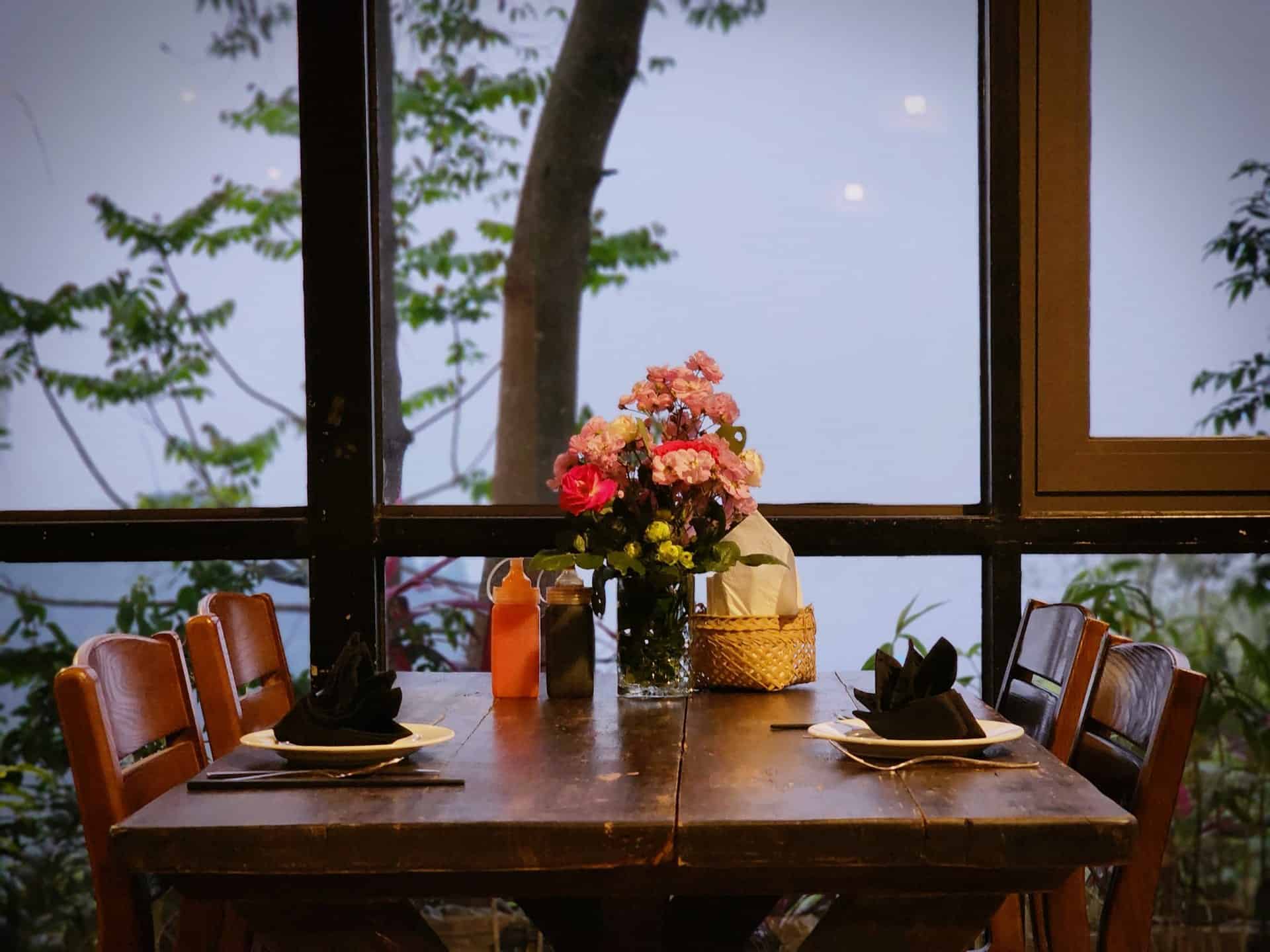 Phòng nghỉ TVPalm Ecolodge Hà Giang 9 Bàn ăn gỗ với bình hoa tươi cạnh cửa kính nhìn ra biển mây tại The Palm Restaurant