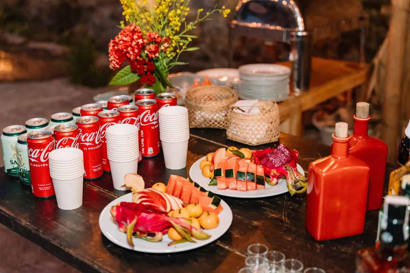 Phòng nghỉ TVPalm Ecolodge Hà Giang 12 Đĩa trái cây tươi, nước uống và bình gốm đỏ trên bàn gỗ tại TVPalm Ecolodge