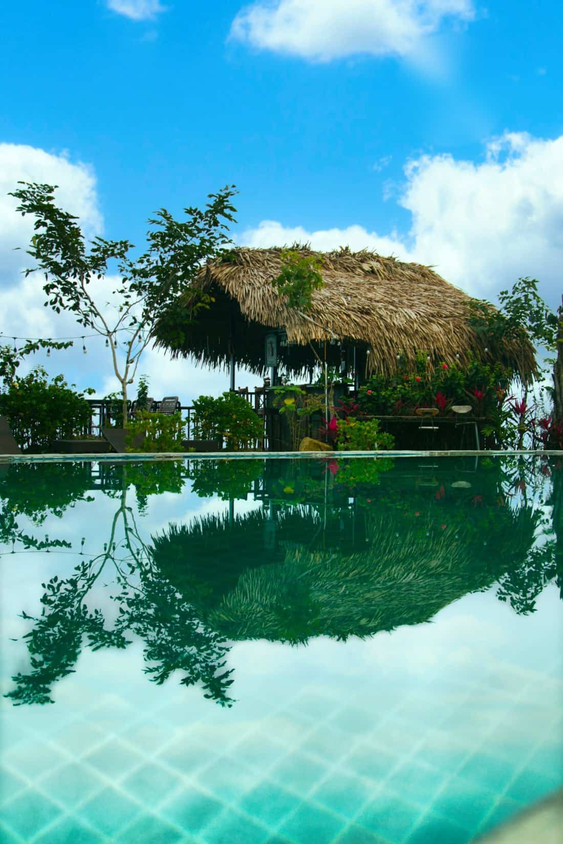 Phòng nghỉ TVPalm Ecolodge Hà Giang 16 Mặt nước bể bơi phản chiếu quán bar mái lá và bầu trời tại TVPalm Ecolodge