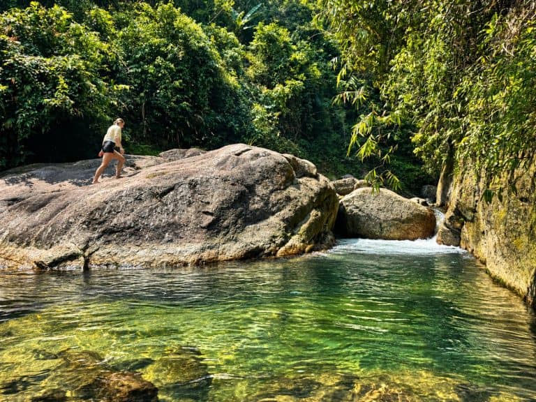 Trekker climbing a boulder beside a forest stream pool
