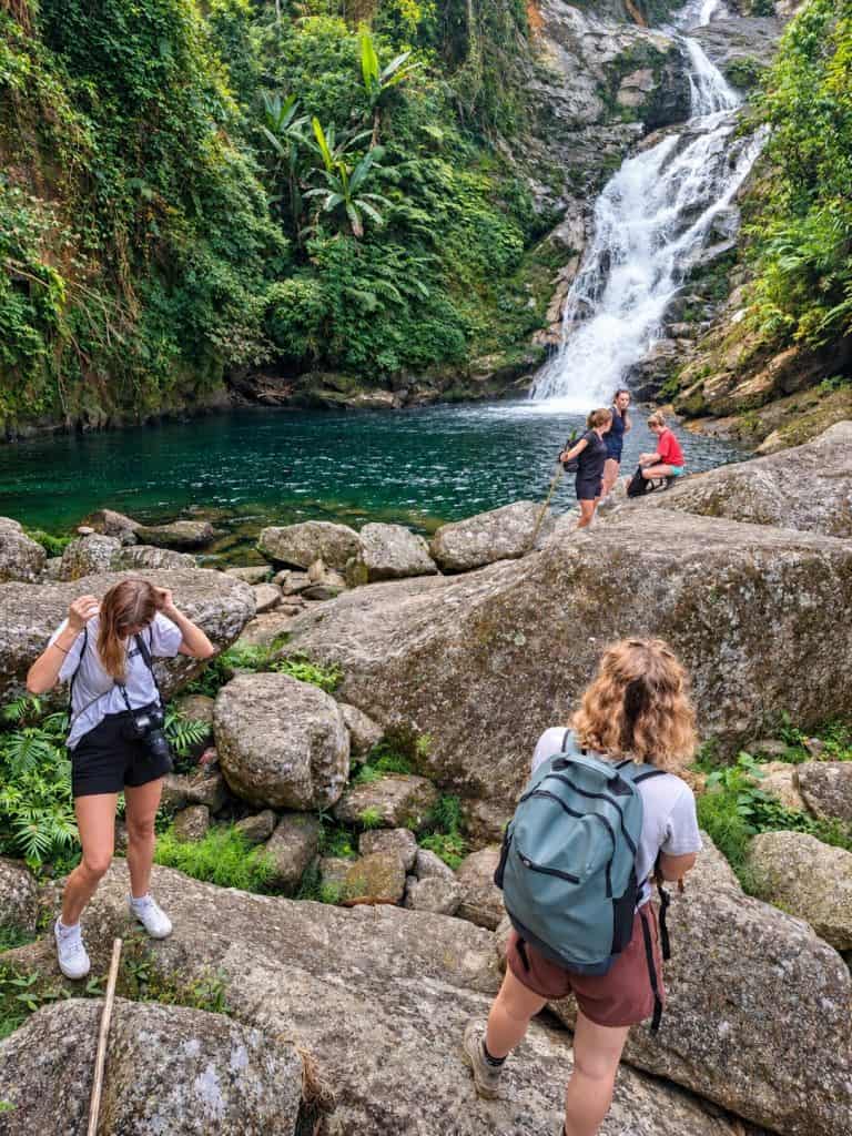 Trekkers on the boulders below a forest waterfall on the Tay Con Linh trek
