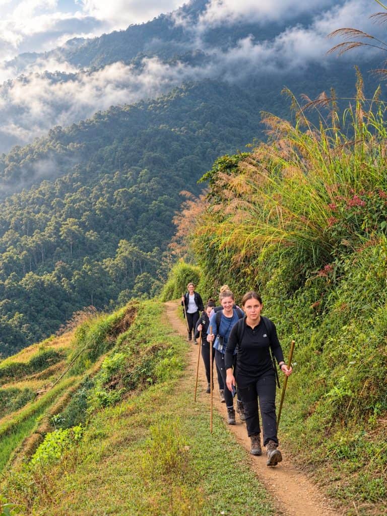 Trekkers climbing a ridge trail with clouds over the forest of Tay Con Linh