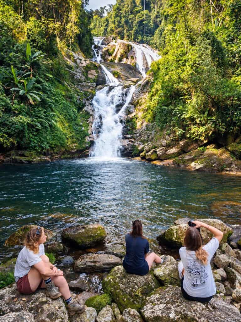 Trekkers sitting on rocks in front of a waterfall