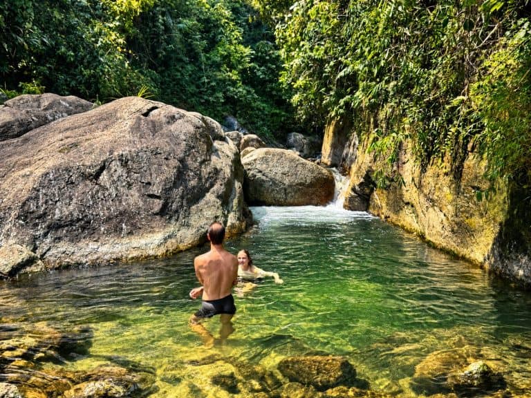 Two trekkers swimming in a clear forest stream pool