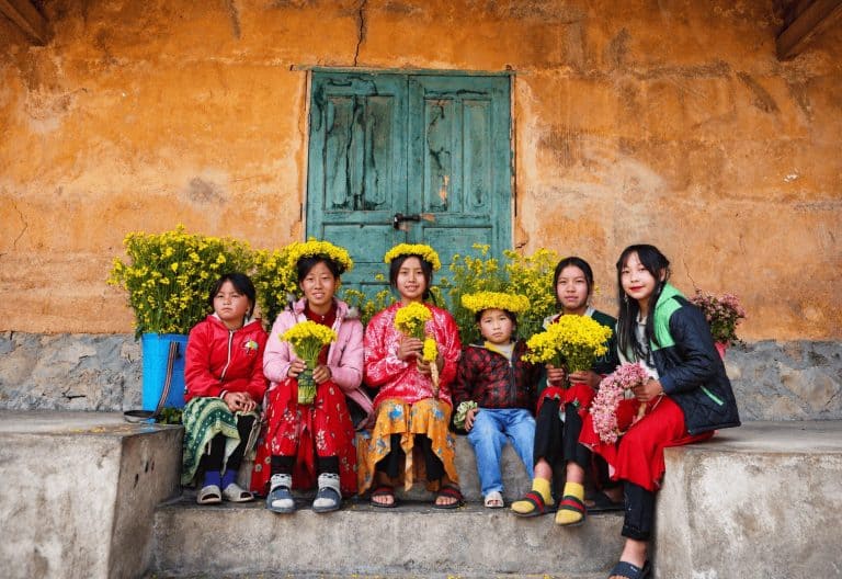 Village children holding yellow flowers in front of an earthen house