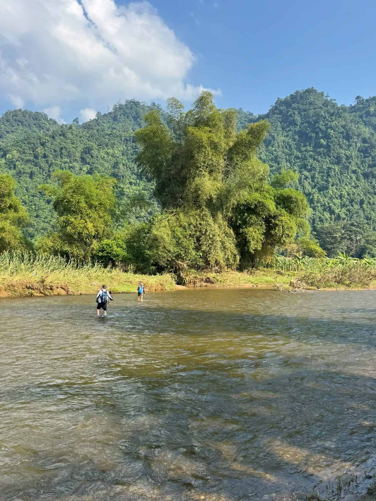 Trekkers wading a clear river on the way into Tung Ba forest, Ha Giang