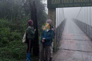 Tourists pose with local sign near Dao Ao Dai Villages suspension bridge